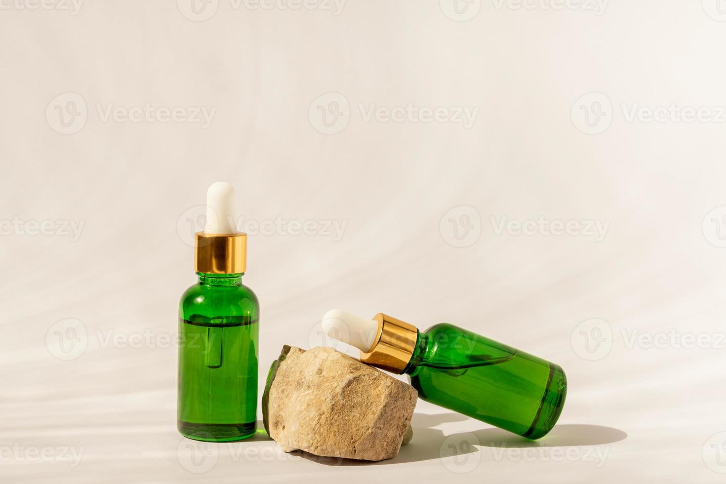 verde bicchiere cosmetico bottiglie con un' contagocce su un' beige sfondo con pietre e tropicale le foglie. naturale cosmetici concetto, naturale essenziale olio e pelle cura prodotti foto