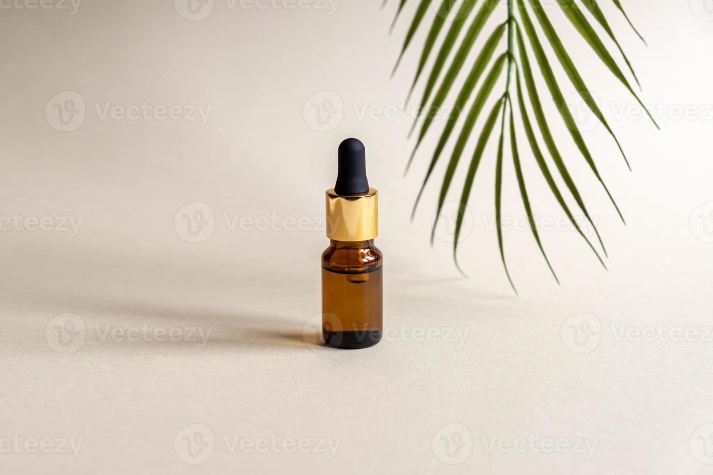 un' bicchiere cosmetico bottiglia con un' contagocce su un' grigio sfondo con palma le foglie. naturale cosmetici concetto, naturale essenziale olio foto