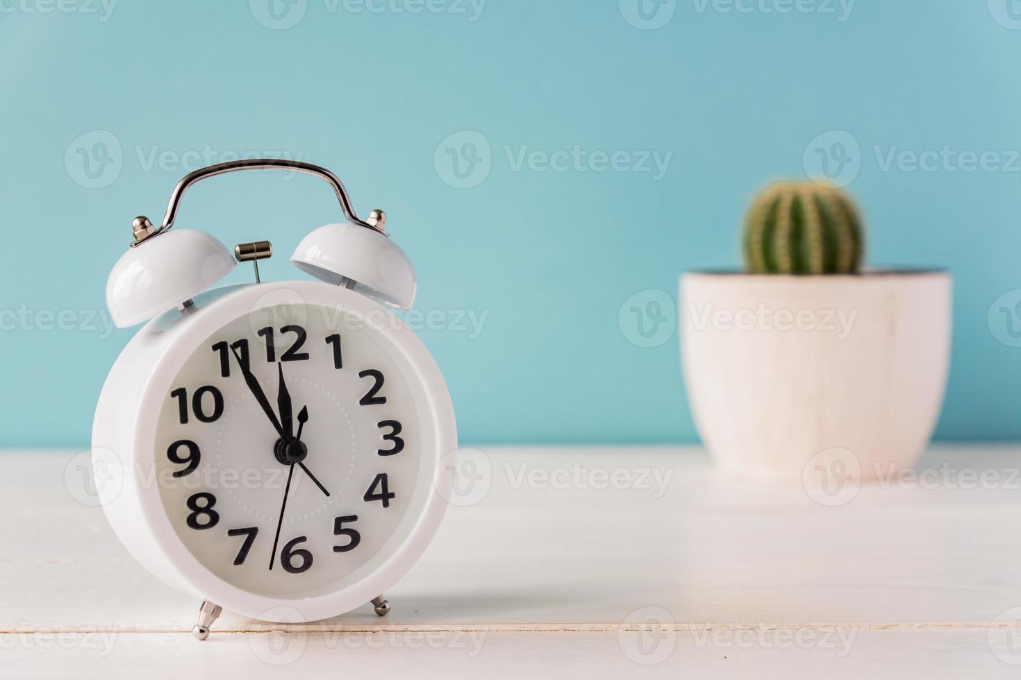 bianca allarme orologio in piedi su un' di legno mensola su verde sfondo. cactus nel un' pentola su il sfondo. foto