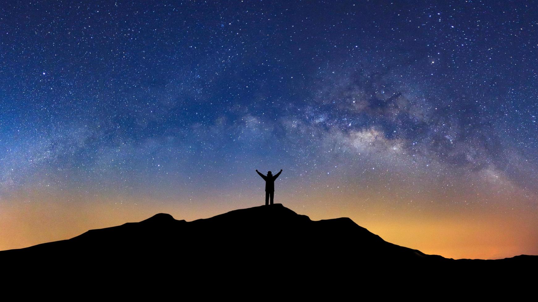 panorama paesaggio con latteo modo, notte cielo con stelle e silhouette di un' in piedi sportivo uomo con sollevato su braccia su alto montagna. foto