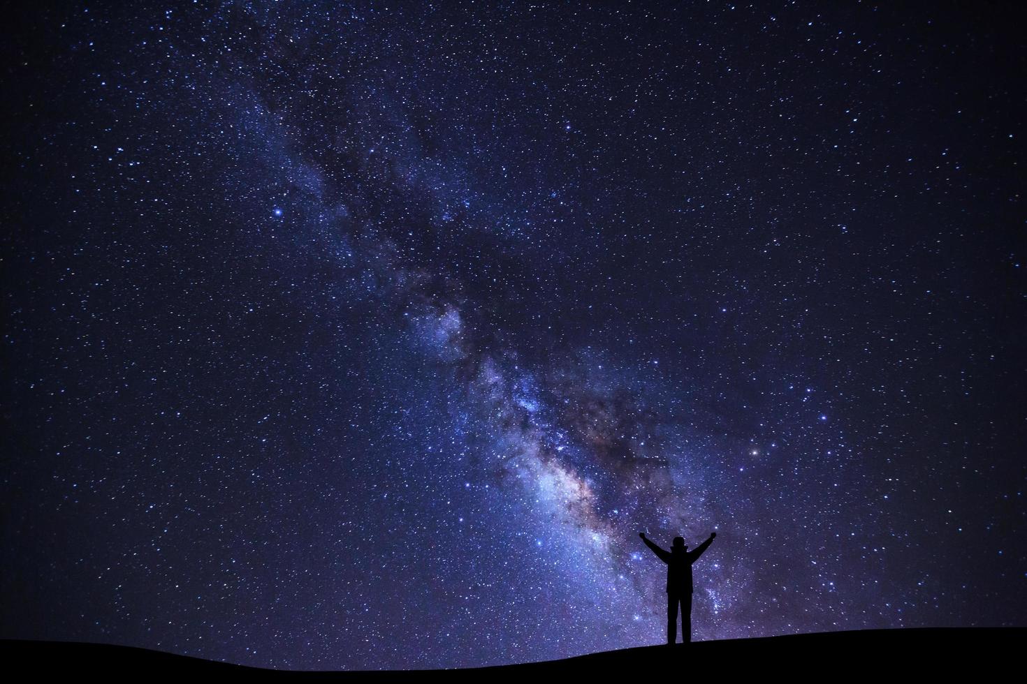 paesaggio con latteo modo galassia, stellato notte cielo con stelle e silhouette di un' in piedi sportivo uomo con sollevato su braccia su alto montagna. foto