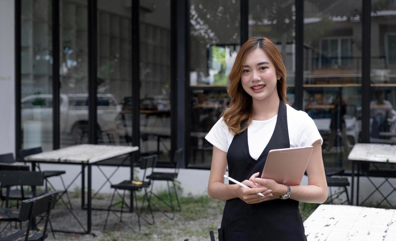 ritratto, bellissimo del Millennio asiatico femmina cameriera o ristorante proprietario in piedi nel davanti di sua ristorante Entrata. ristorante o caffè negozio attività commerciale proprietario concetto. foto