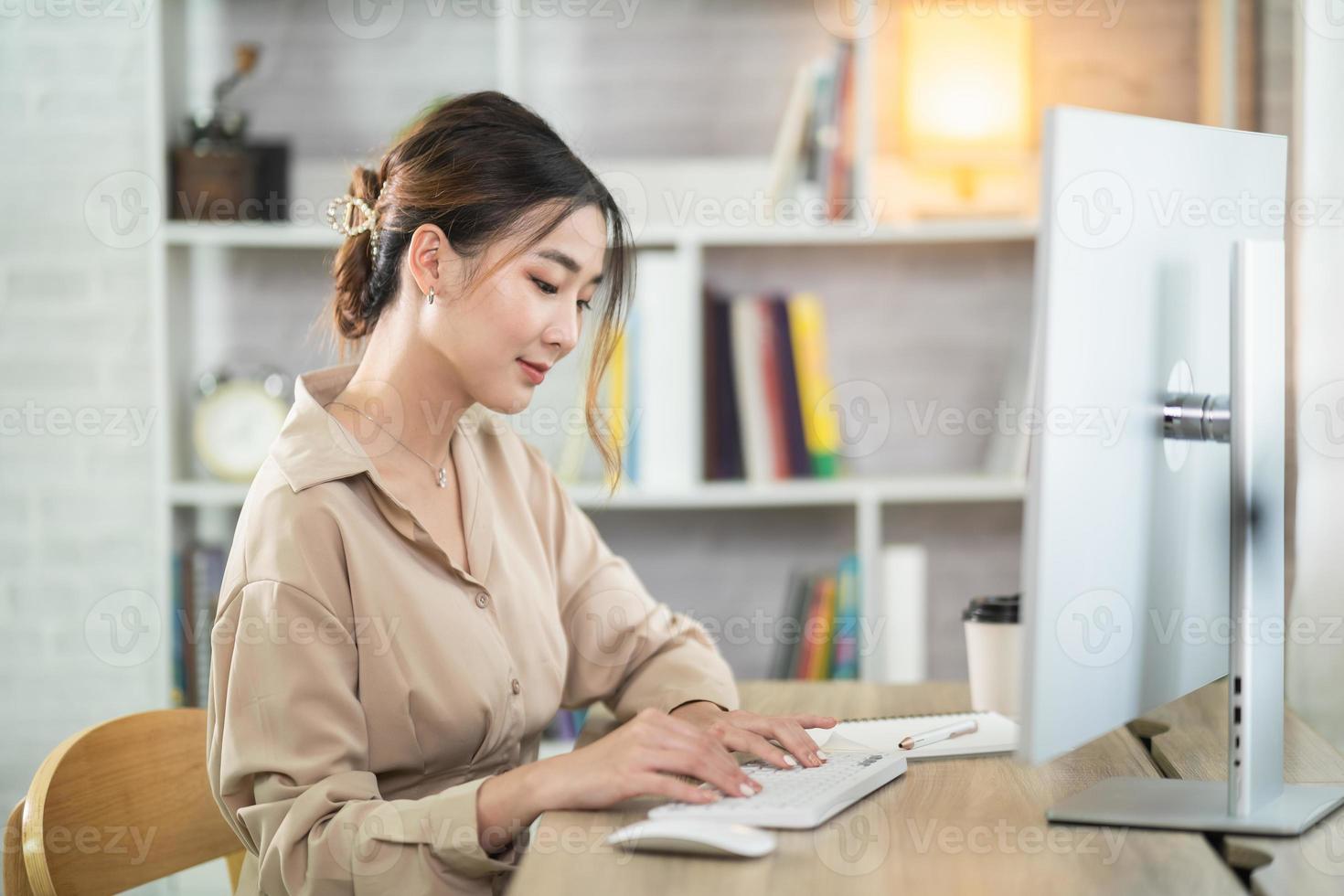 asiatico libero professionista donna sorridente digitando su tastiera e Lavorando su il computer portatile su di legno tavolo a casa. imprenditore donna Lavorando per sua attività commerciale a vivente camera casa. attività commerciale opera a casa concetto. foto