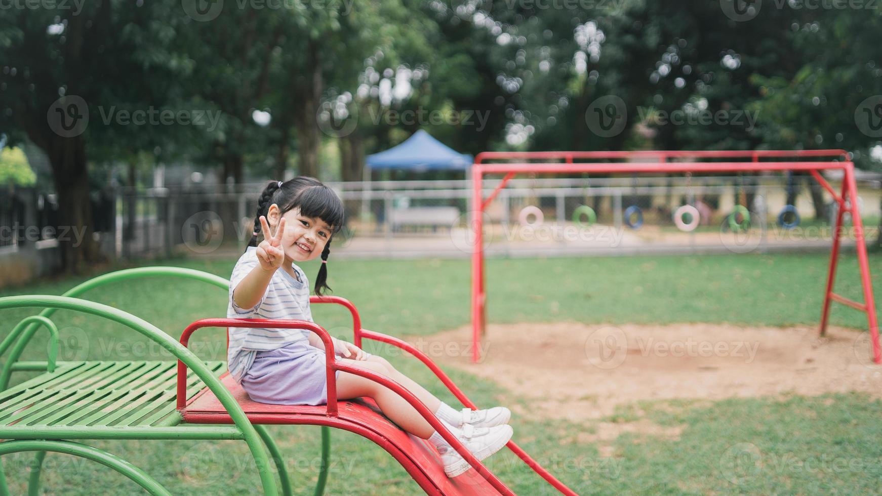 ragazza asiatica carina gioca a scuola o nel cortile dell'asilo o nel parco giochi. sana attività estiva per i bambini. piccola ragazza asiatica che si arrampica all'aperto al parco giochi. bambino che gioca nel parco giochi all'aperto. foto