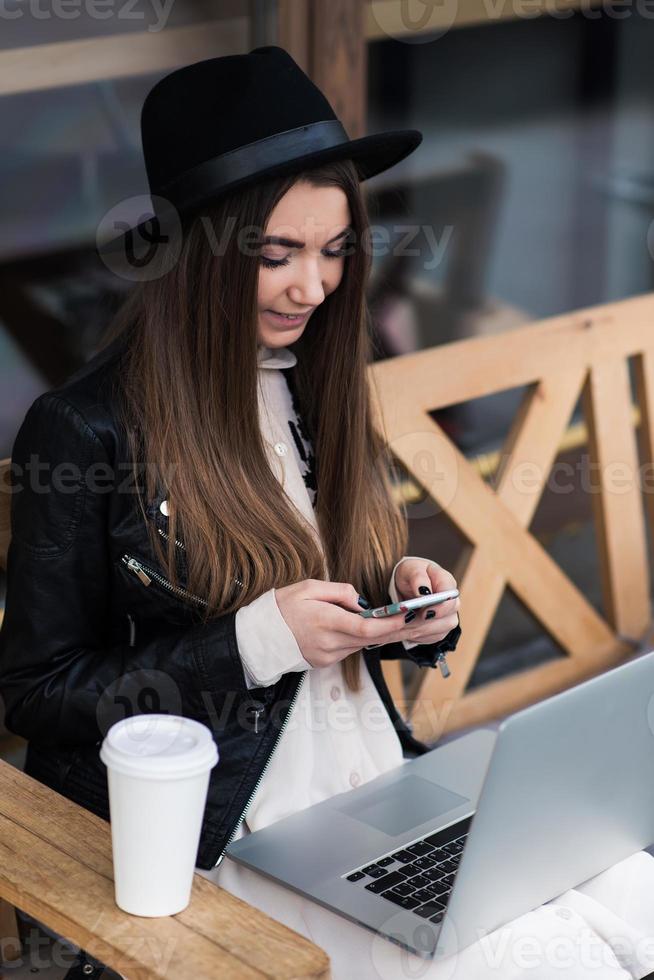 ragazza che scrive testo sul telefono cellulare durante il lavoro su net-book foto