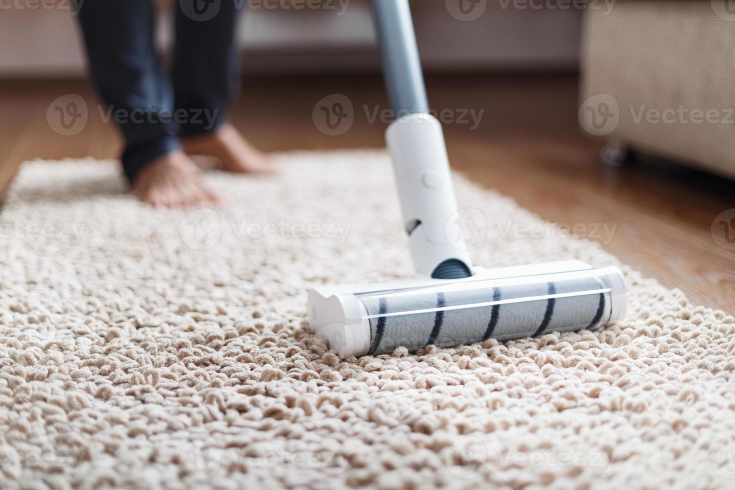un' cordless vuoto addetto alle pulizie pulisce il tappeto nel il vivente camera con il parte inferiore di il gambe. moderno tecnologie per pulizia il Casa foto