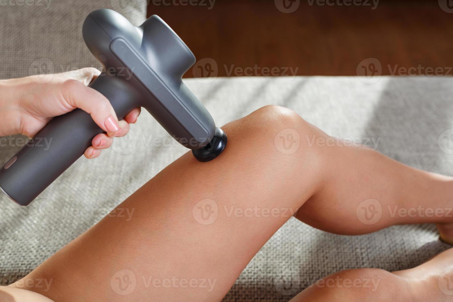 un' donna massaggi sua gambe con un automatico pistola a casa. foto