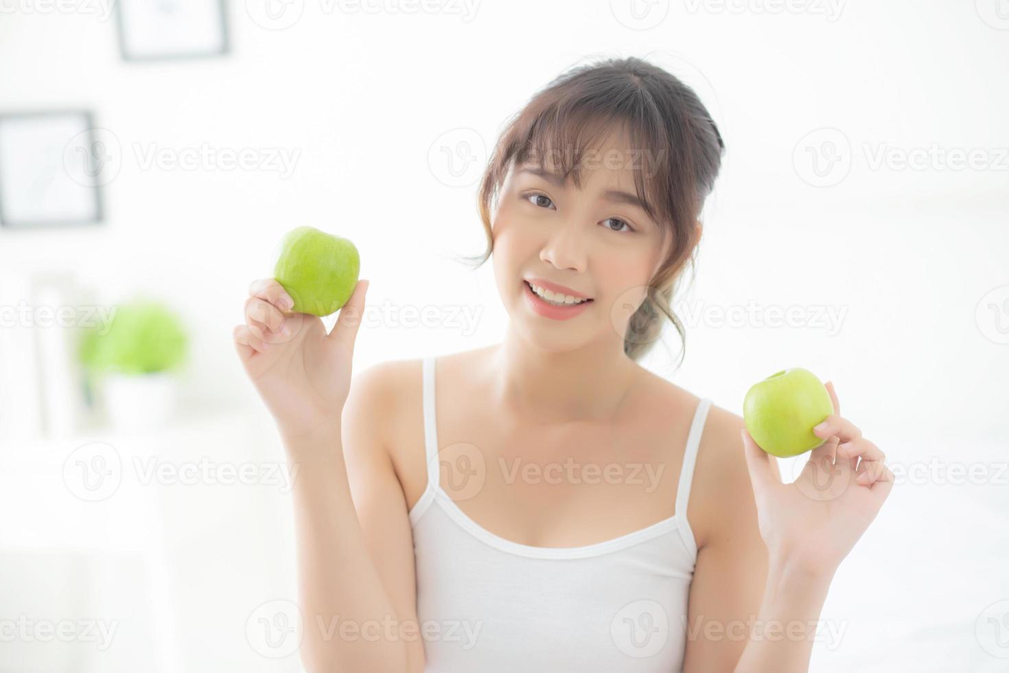 bellissimo ritratto giovane donna asiatica che tiene e mangia frutta mela verde in camera da letto a casa, stile di vita di nutrizione ragazza sana e cura perdita di peso, concetto di salute e benessere. foto