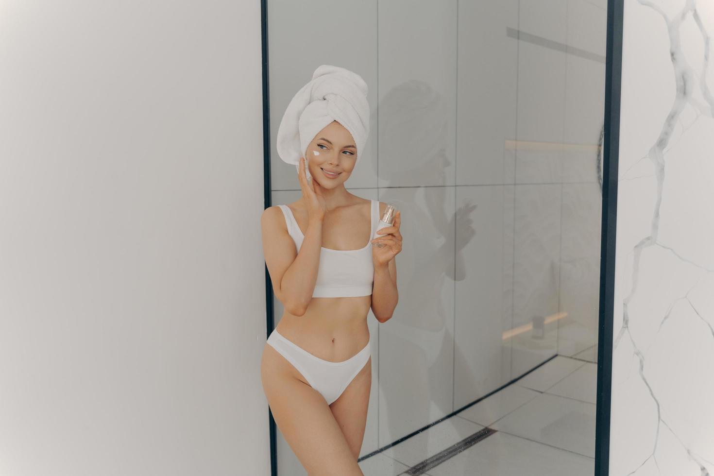 immagine di una bella ragazza con un asciugamano sulla testa che tiene una crema idratante per il viso foto