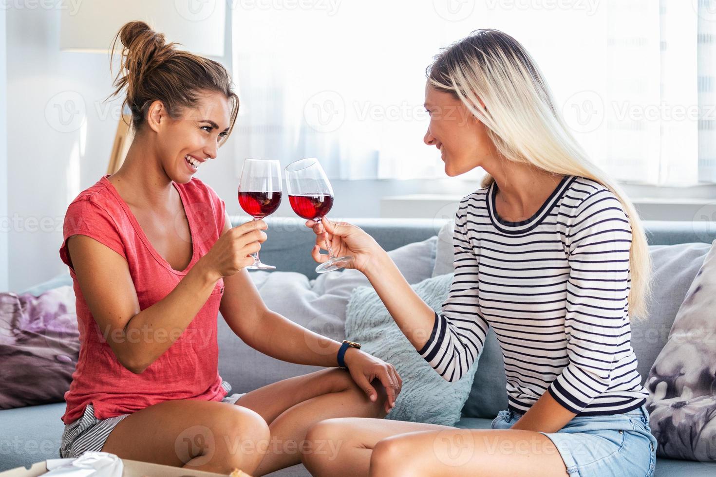 Due attraente ragazze, allegro migliore amici avendo divertimento e potabile rosso vino a casa. Due bicchieri di bianca vino nel mani foto