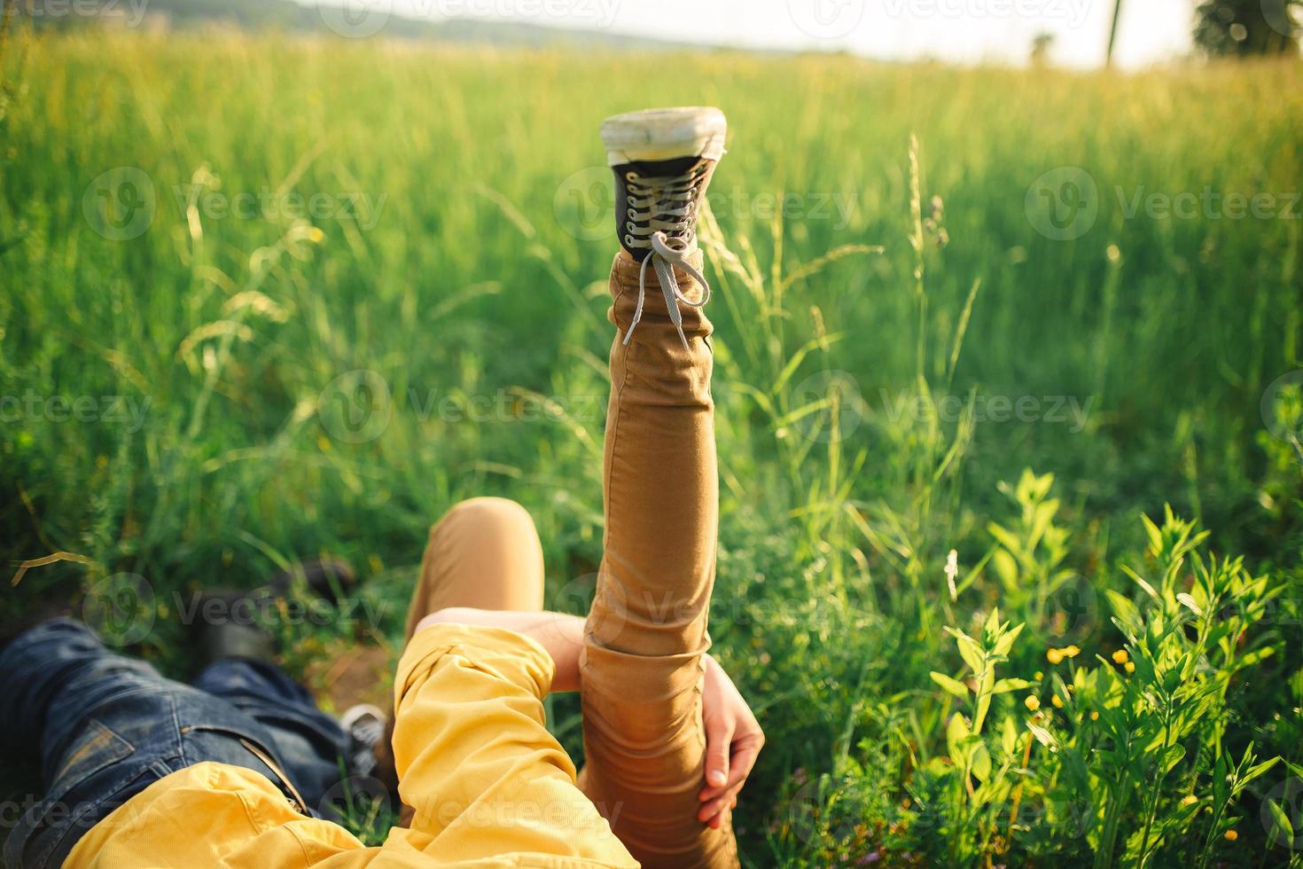 donna e uomo avendo divertimento all'aperto. amorevole fricchettone coppia a piedi nel il campo, baci e Tenere mani, abbracciare, dire bugie nel il erba e sollevamento loro gambe su nel il estate a tramonto. san valentino giorno foto