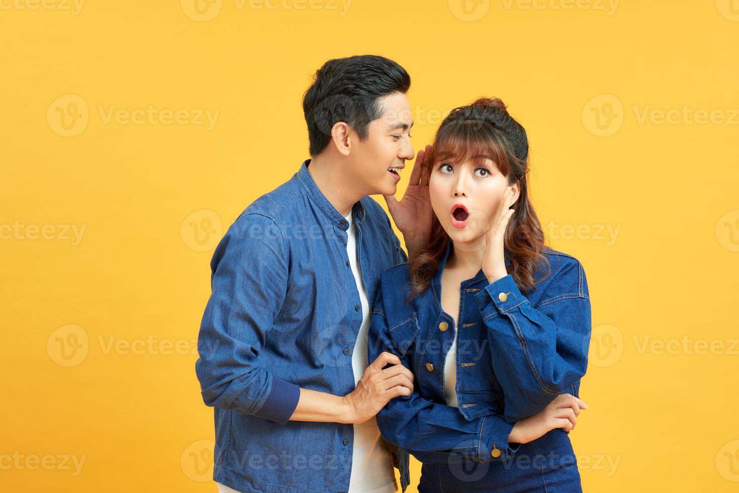 Immagine di bello uomo sussurrando segreto o interessante pettegolezzo per donna nel sua orecchio isolato al di sopra di giallo sfondo foto
