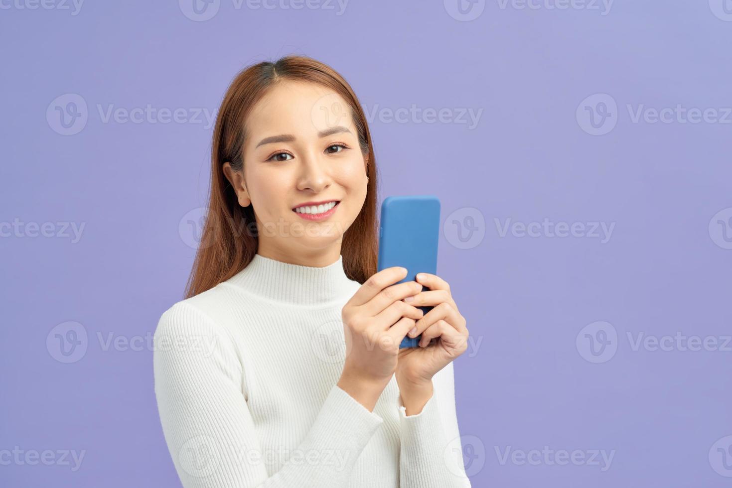 sorridente bello giovane donna in piedi e utilizzando cellula Telefono al di sopra di viola sfondo foto