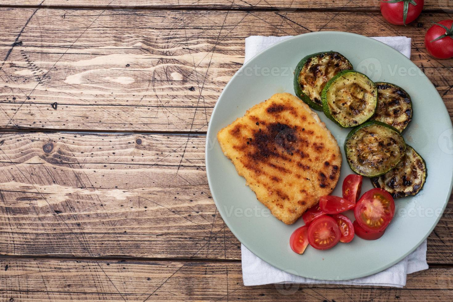 cotoletta di pollo e zucchine cucinato su il griglia. fresco pomodori su un' piatto. pronto delizioso cena il pranzo. di legno sfondo copia spazio. foto