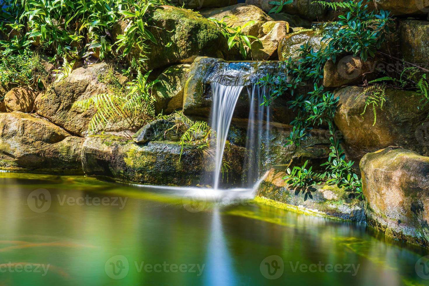 giapponese giardino cascate. lussureggiante verde tropicale koi stagno con cascata a partire dal ogni lato. un' lussureggiante verde giardino con cascata a cascata giù il roccioso pietre. zen e tranquillo, calmo sfondo. foto
