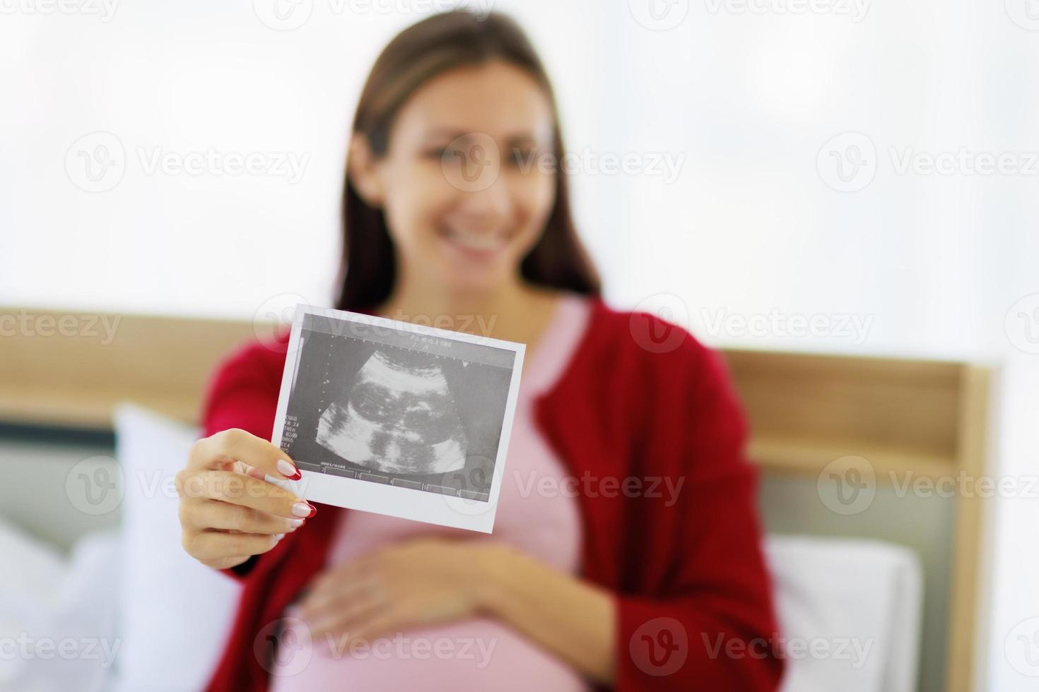 bellissimo caucasico madre felicemente e animatamente Tenere ultrasuono immagini su sua letto nel sua Camera da letto foto