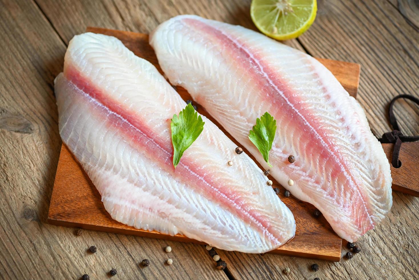 pesce filetto su di legno tavola con ingredienti per cucinando, fresco crudo pangasio pesce filetto con erba e spezie nero Pepe Limone lime, carne dolly pesce Tilapia a strisce pesce gatto foto