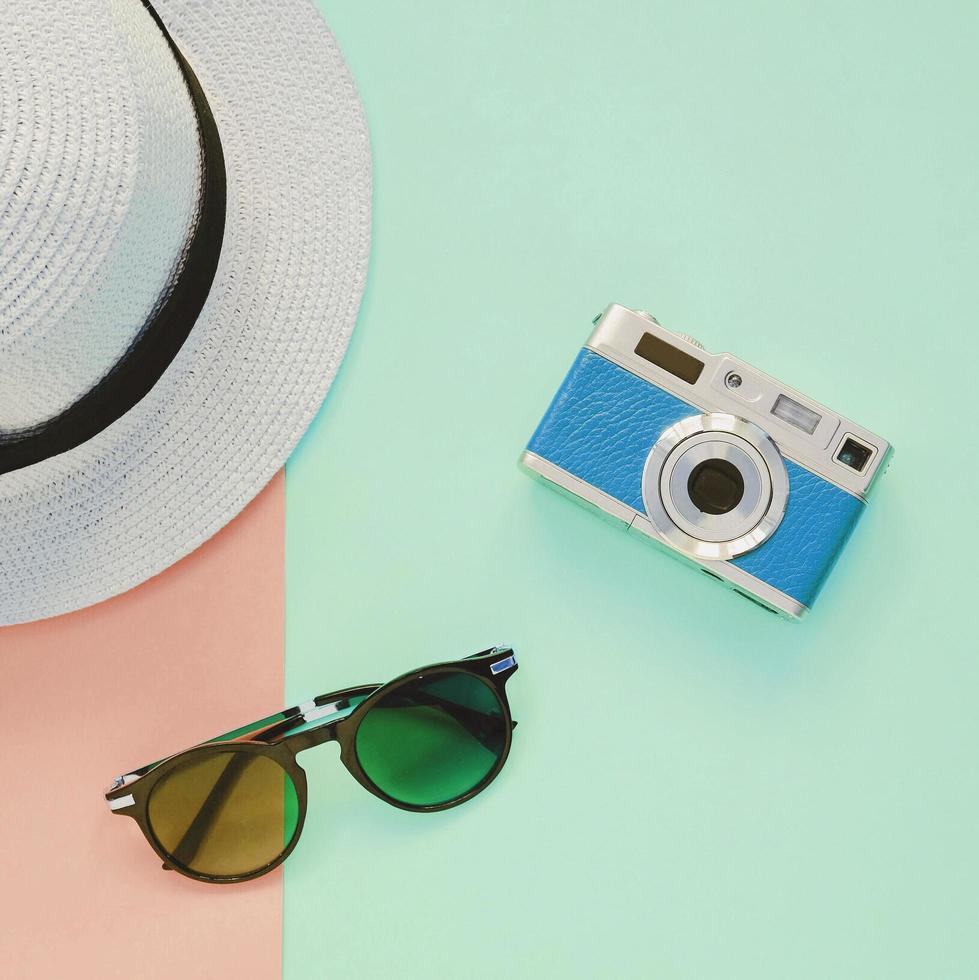 creativo piatto posare moda stile con telecamera, occhiali da sole e Panama cappello su pastello colore sfondo foto