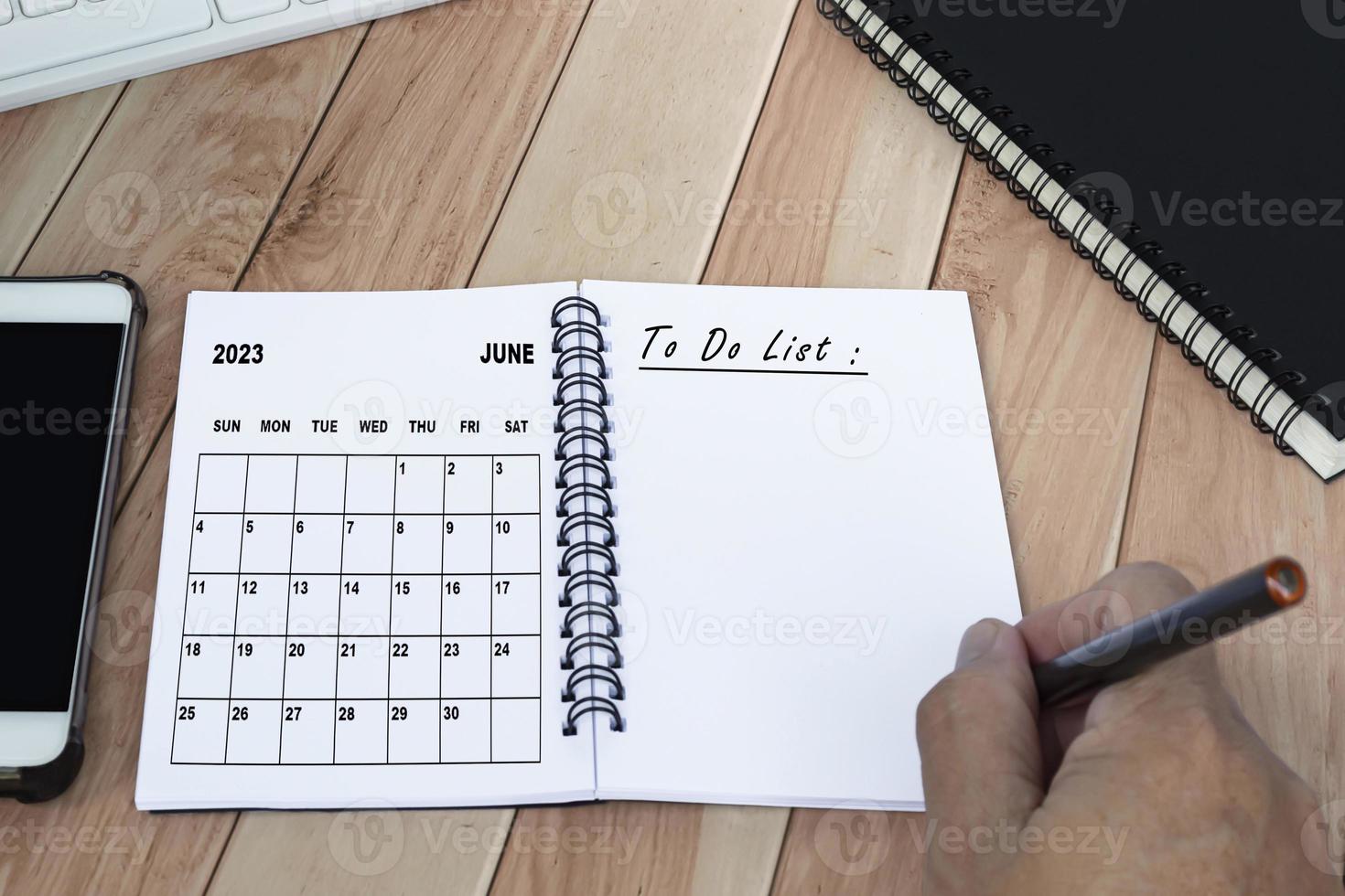 mani con penna scrittura per fare elenco con giugno 2023 calendario su taccuino. foto