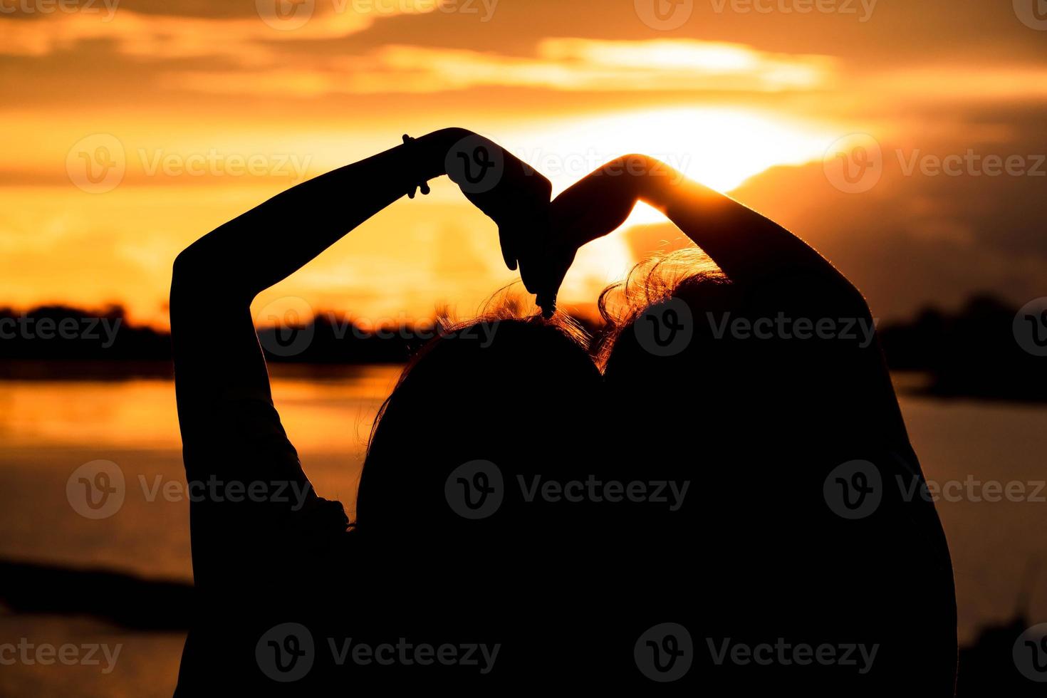 silhouette donna fabbricazione a forma di cuore mani con Alba vicino il forma e lago sfondo, amore concetto. contento San Valentino giorno foto