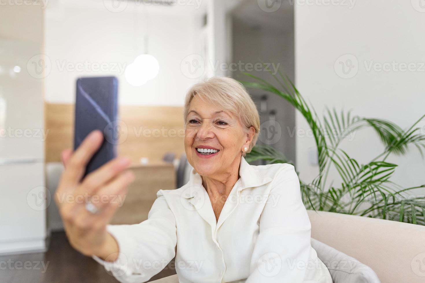 nonna assunzione selfie a casa nel il soggiorno. vicino su ritratto di contento allegro delizioso affascinante bellissimo anziano signora nonna nonna assunzione un' autoscatto. vecchiaia, la pensione e persone concetto foto
