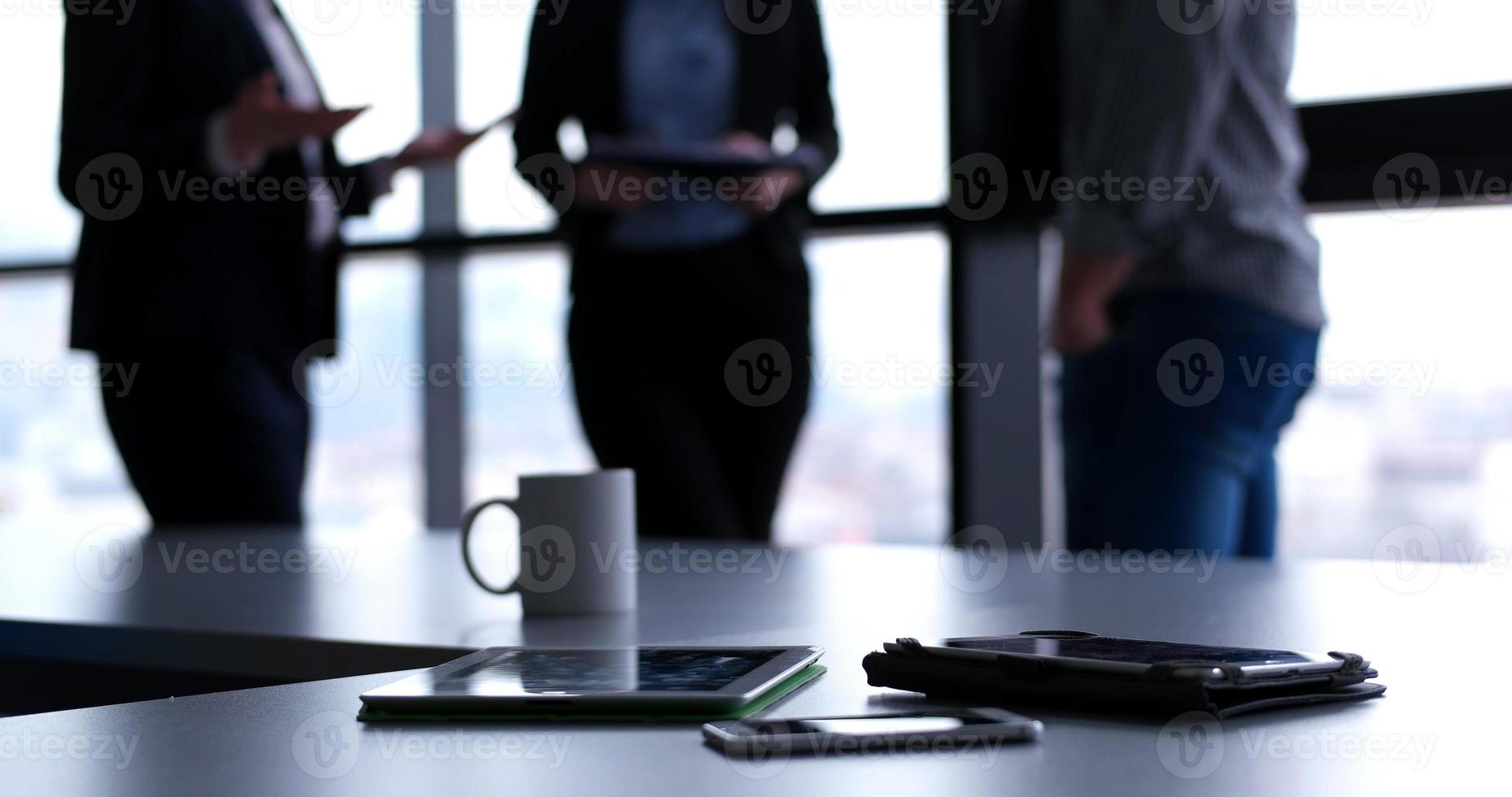 tavoletta, mobile cellula Telefono e tazza di caffè nel ufficio con attività commerciale persone nel backgorund foto