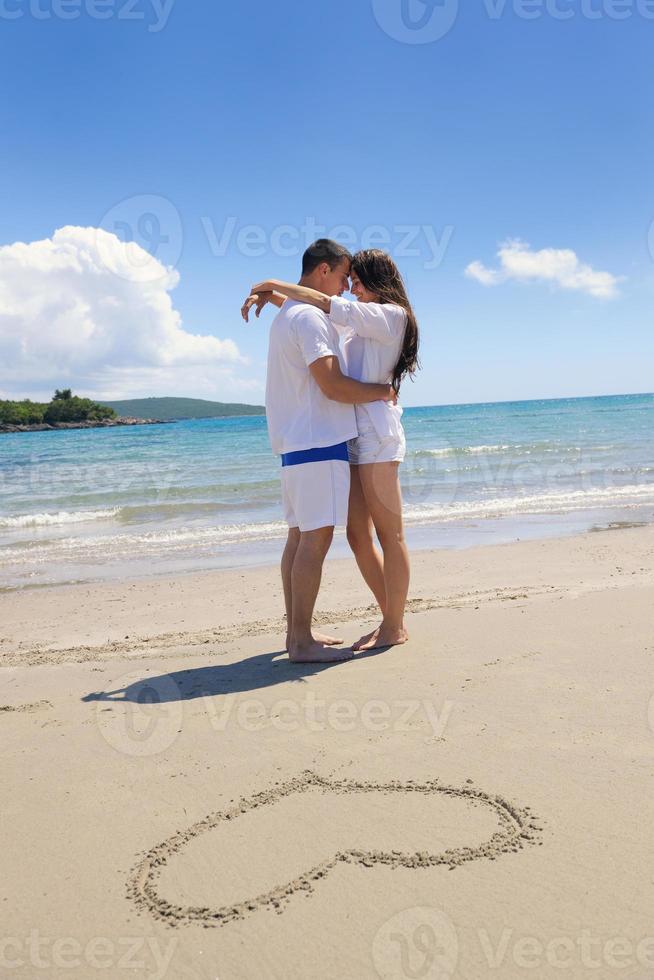 romantico coppia nel amore avere divertimento su il spiaggia con cuore disegno su sabbia foto