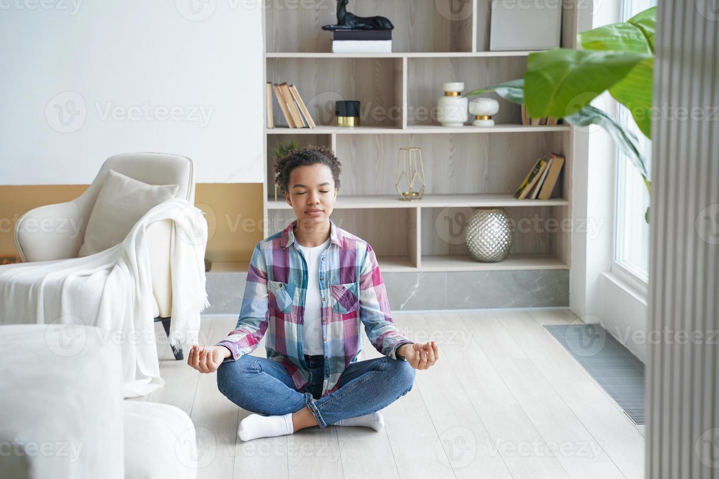ragazza afro adolescente sta praticando yoga a casa ed esercita la posizione del loto. alleviare lo stress. foto
