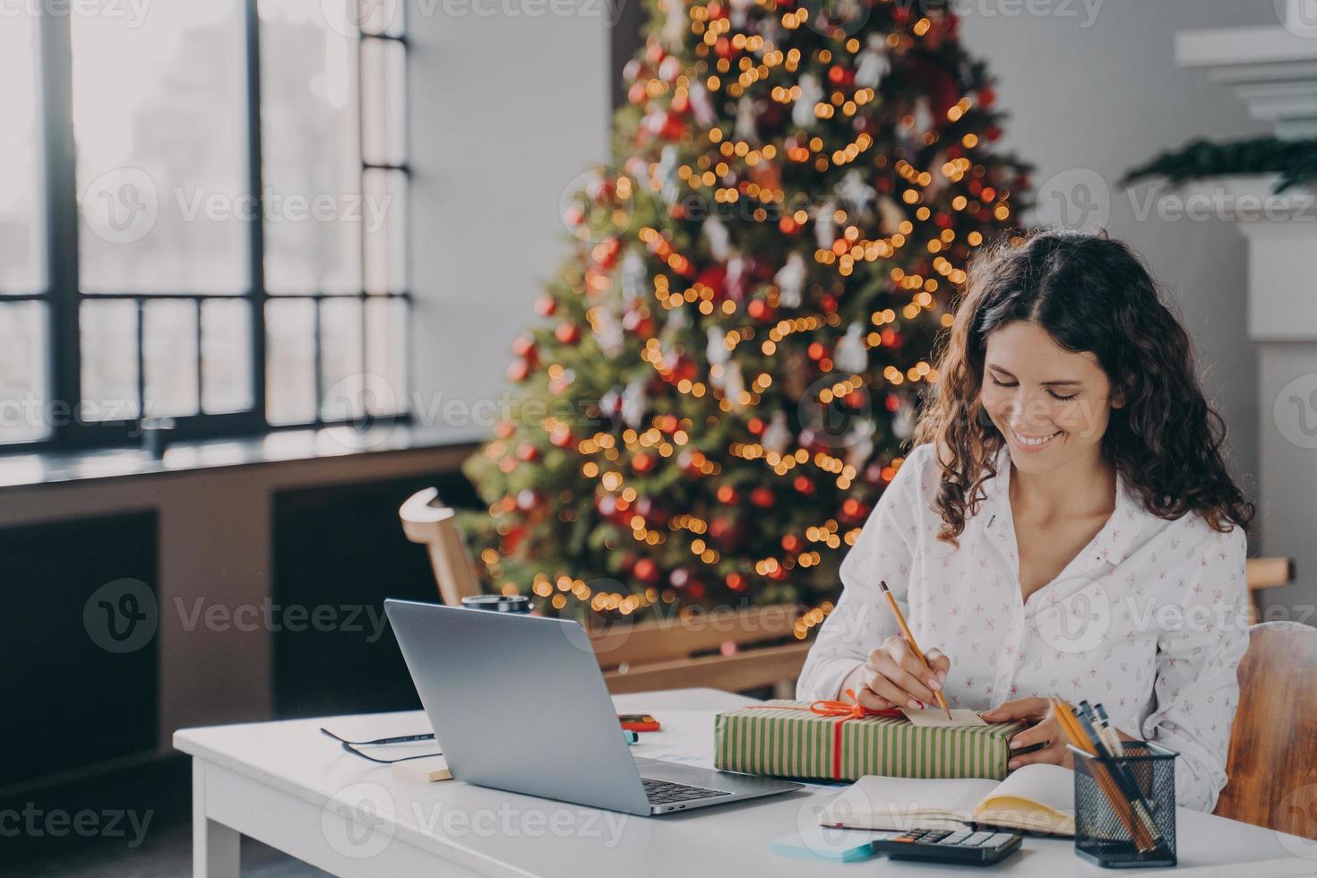 felice donna europea impiegato che scrive lettera di natale, biglietto di auguri con auguri di vacanza foto