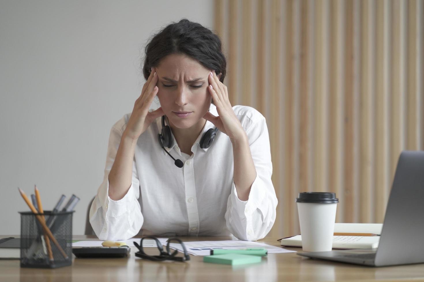 donna imprenditrice stressata che soffre di mal di testa che massaggia le tempie mentre è seduta a casa in ufficio foto