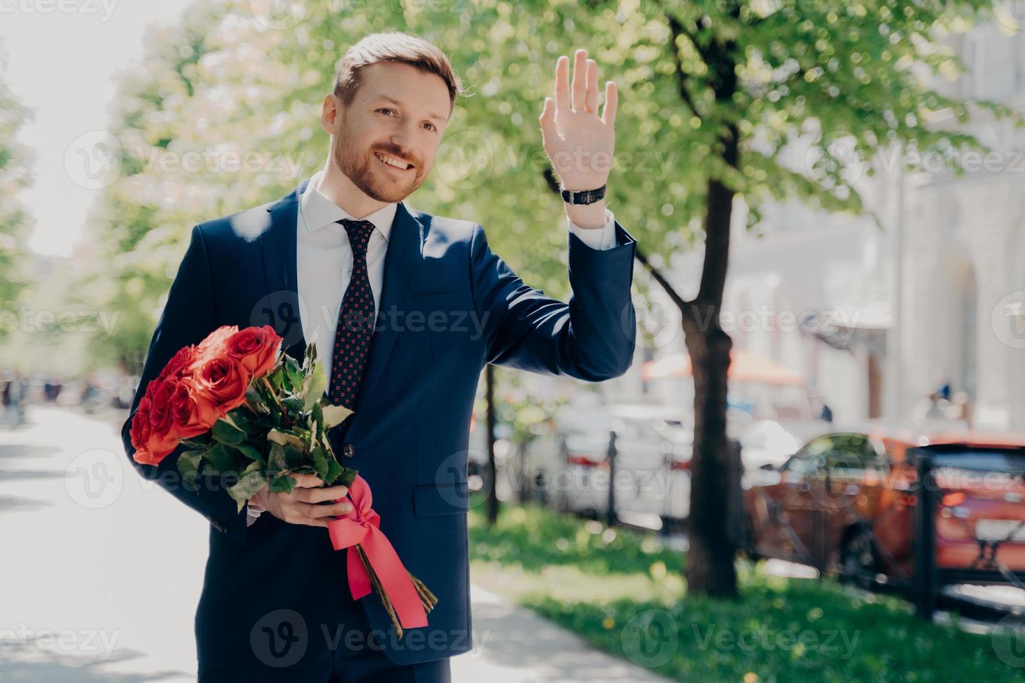 uomo d'affari maschio felice in tuta con bouquet che saluta qualcuno al parco cittadino foto