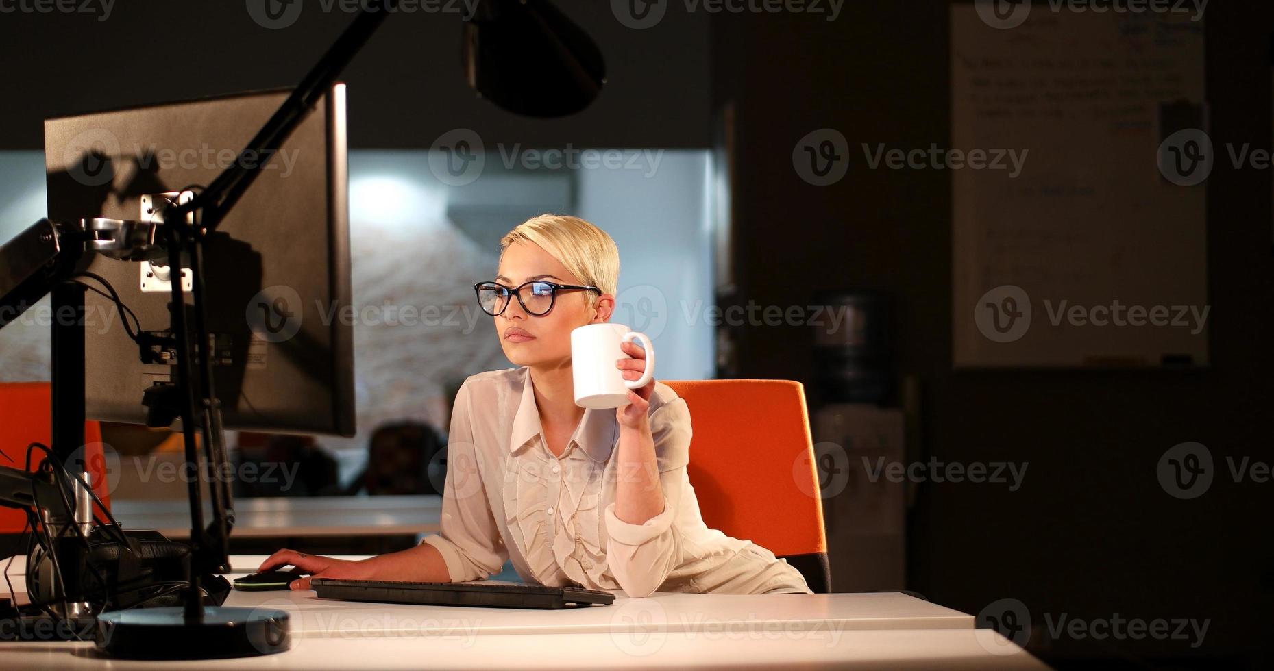 donna Lavorando su computer nel buio ufficio foto