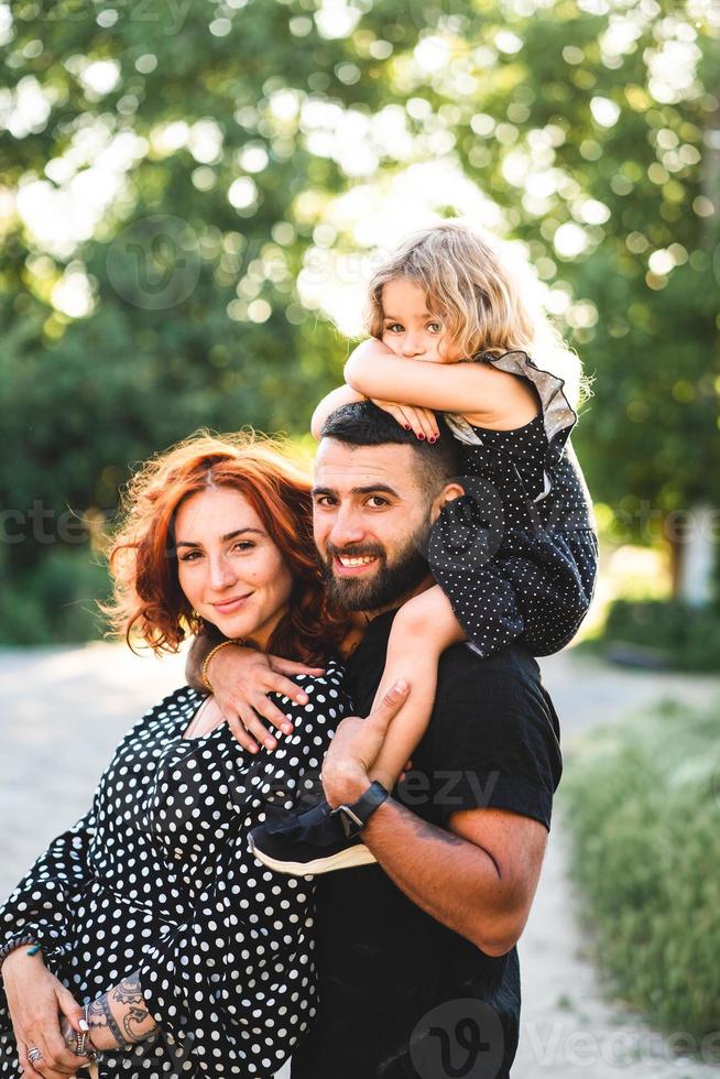 contento genitori con un' piccolo figlia seduta su il le spalle foto