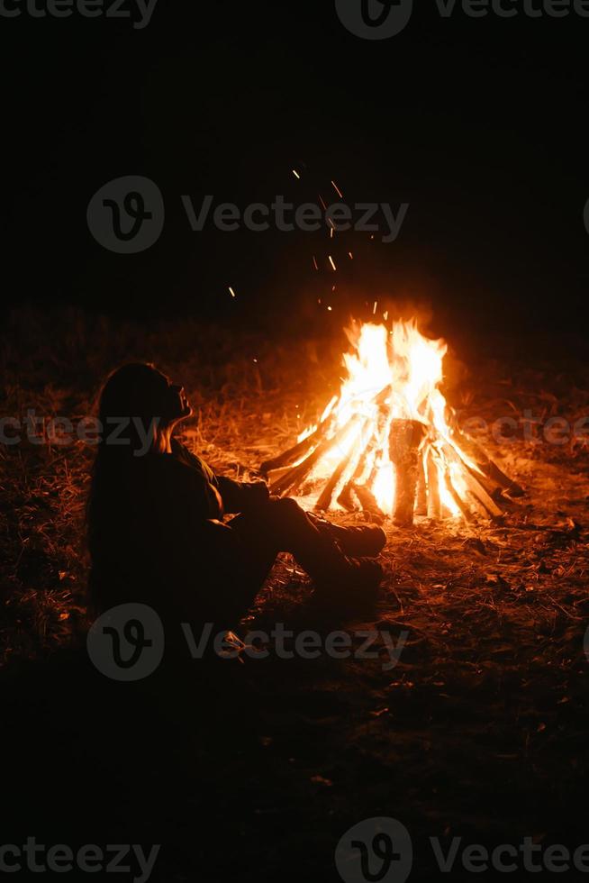 donna seduta e ottenere caldo vicino il falò nel il notte foresta. foto