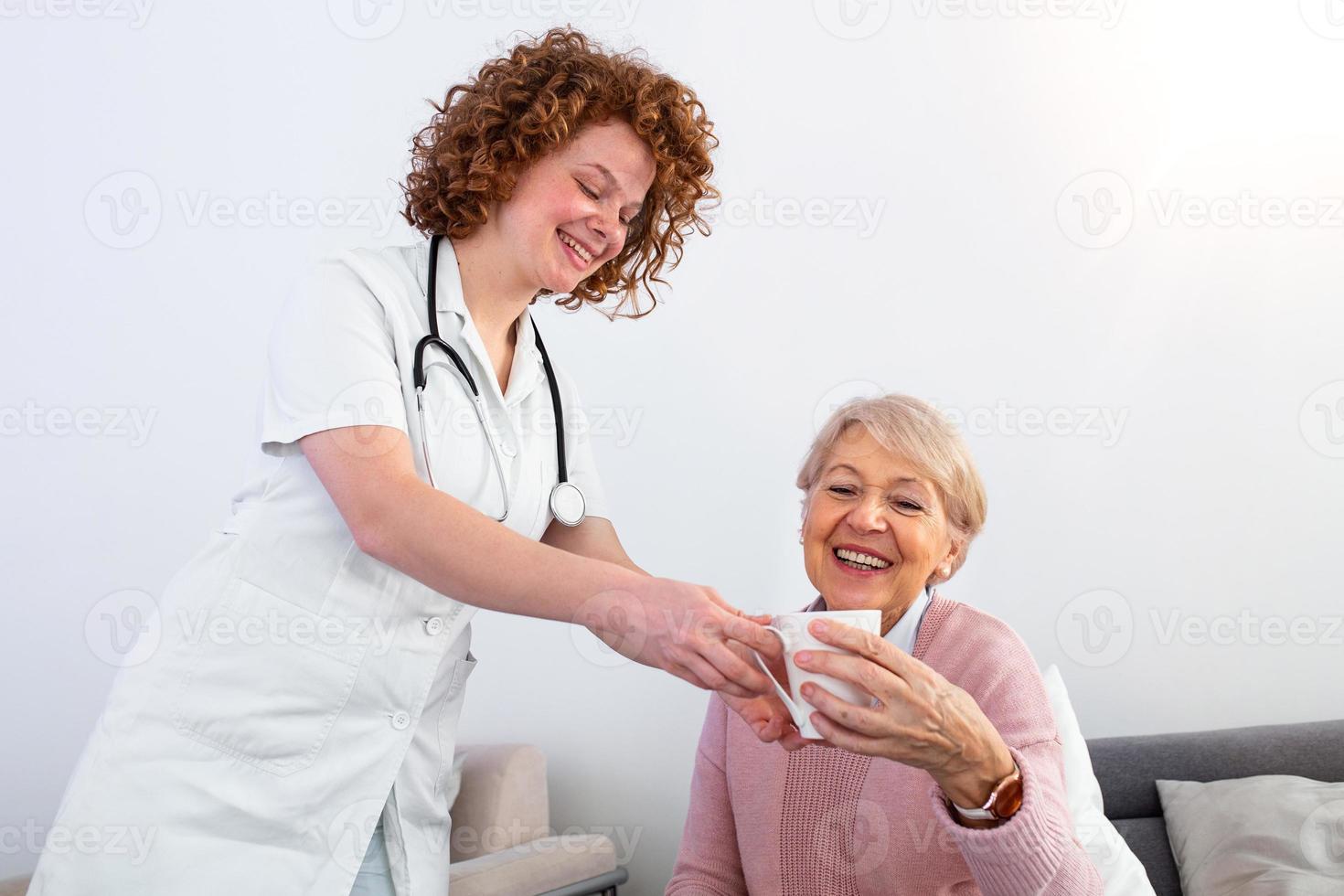 bella giovane badante servendo pomeriggio tazza di tè per più vecchio contento donna. giovane infermiera cura per anziano paziente nel sua casa. demenza e professionale terapia casa badante e anziano adulto donna. foto