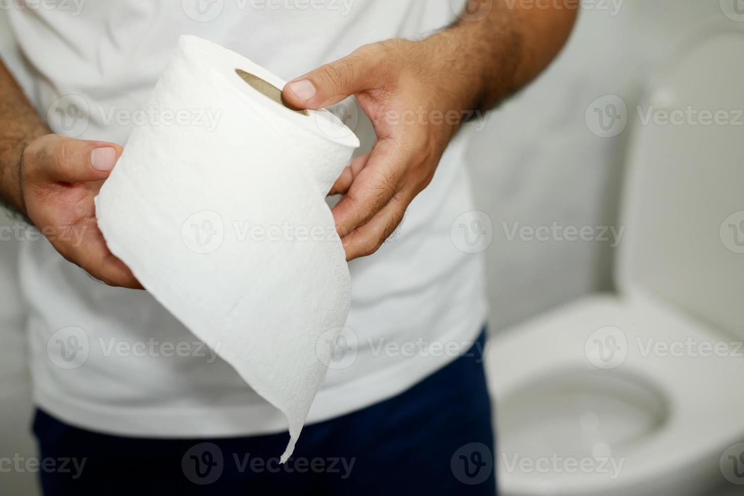 uomo soffre a partire dal diarrea mano hold fazzoletto di carta carta rotolo nel davanti di gabinetto ciotola. stipsi nel bagno. trattamento stomaco dolore e igiene, Salute cura foto