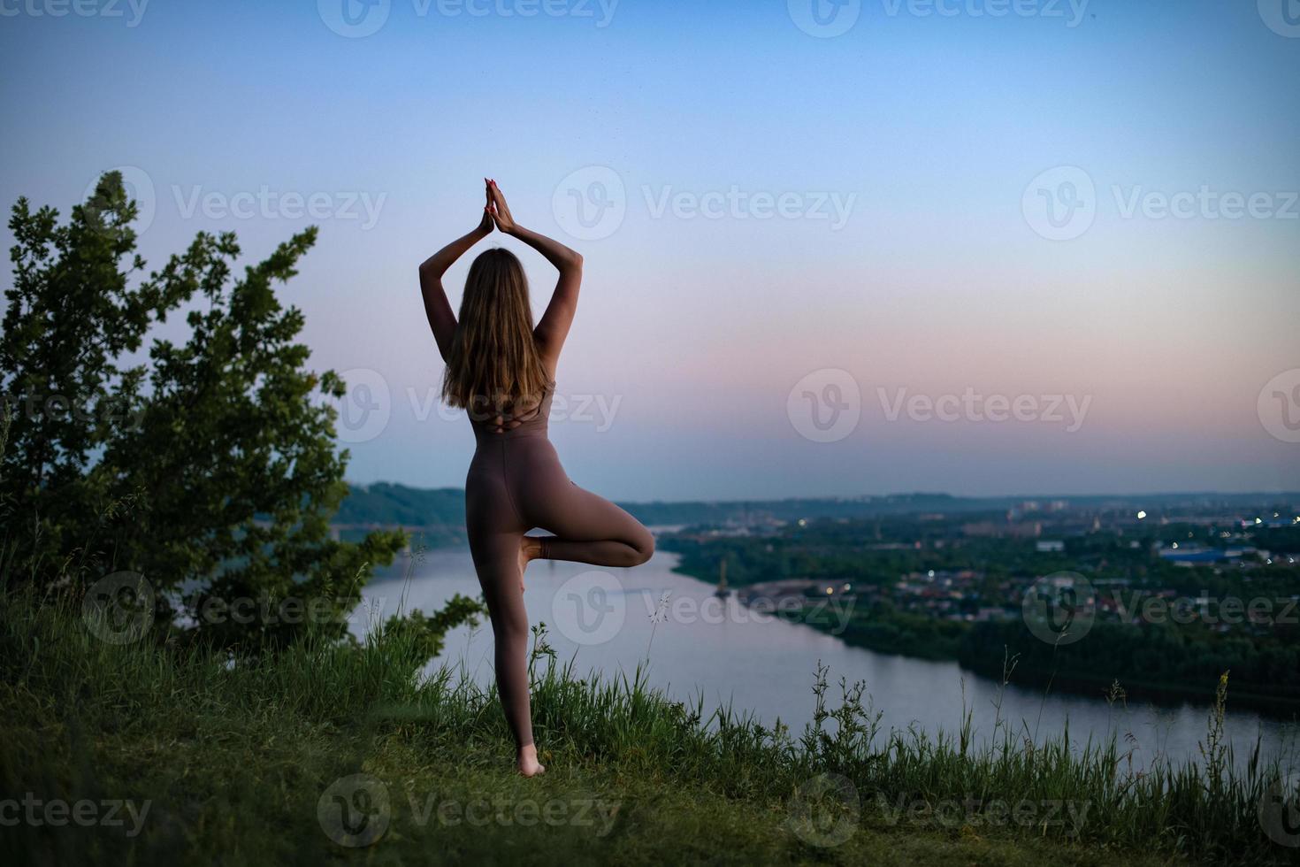 un' giovane ginnasta fa yoga nel natura nel un' parco contro il cielo, utilizzando un' combinazione di tradizionale yoga pose, pilates e dolce danza. connessione con natura. foto