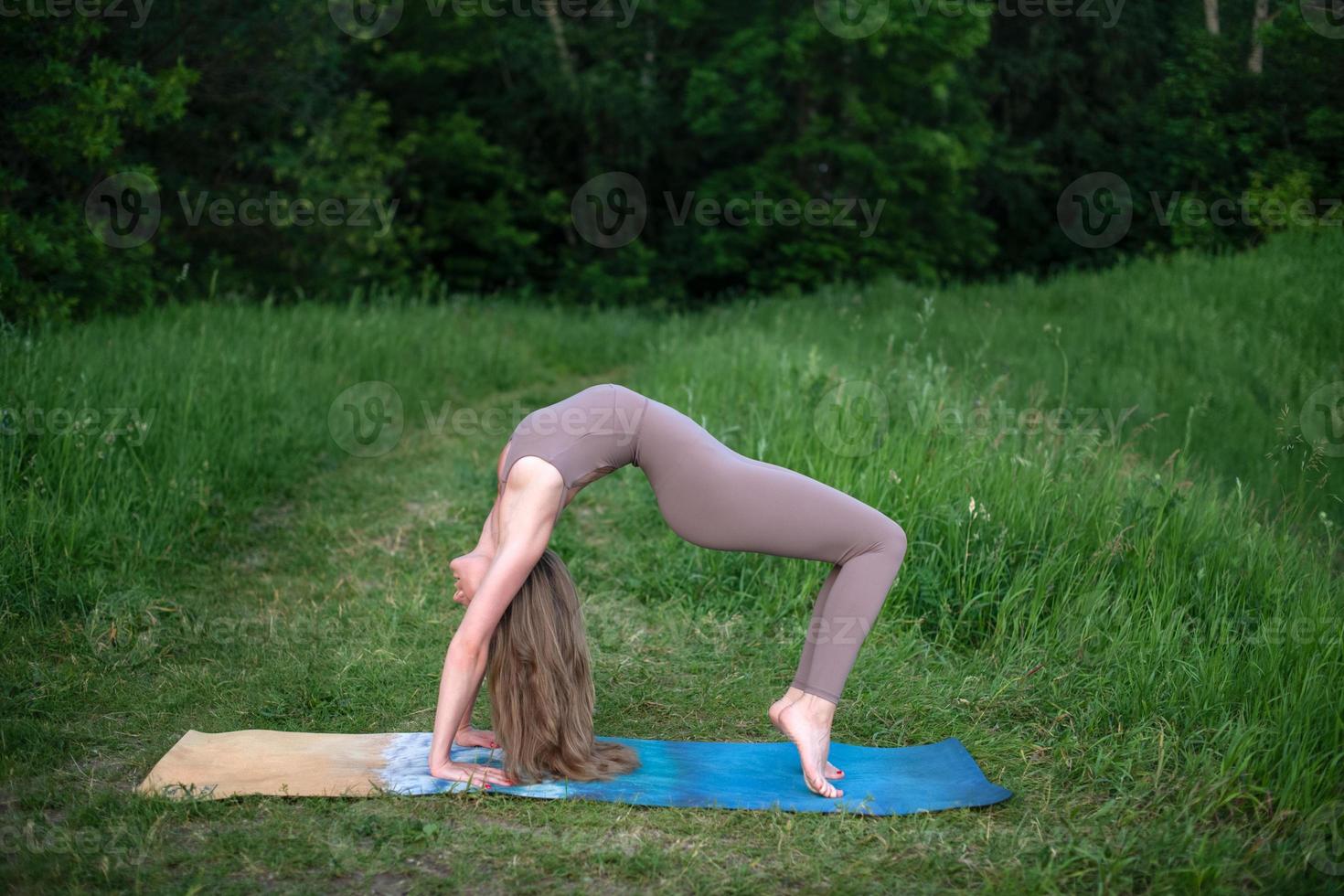 un' giovane ginnasta fa yoga nel natura nel il parco, utilizzando un' combinazione di tradizionale yoga pose, pilates e dolce danza. connessione con natura. foto