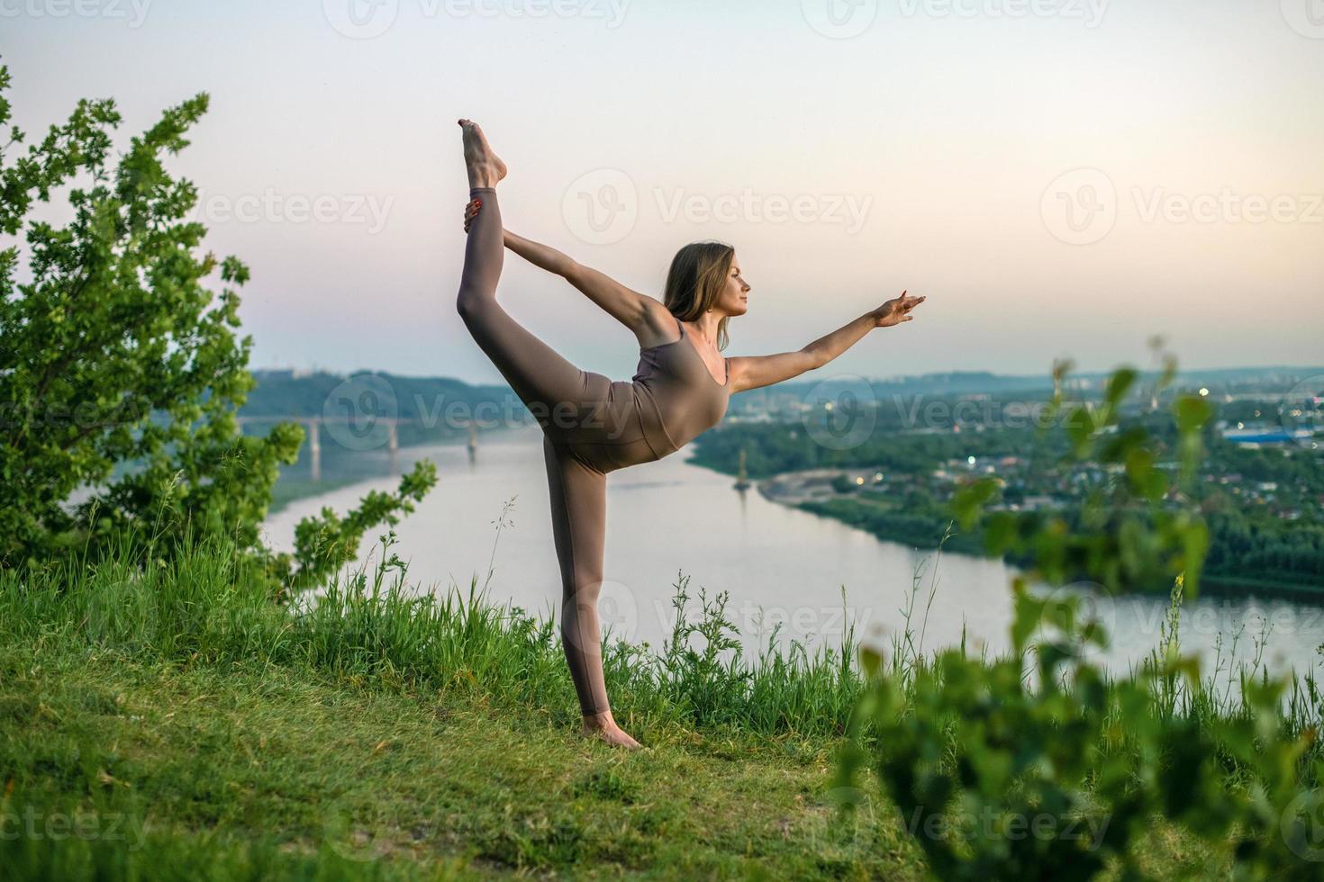 un' giovane ginnasta fa yoga nel natura nel un' parco contro il cielo, utilizzando un' combinazione di tradizionale yoga pose, pilates e dolce danza. connessione con natura. foto