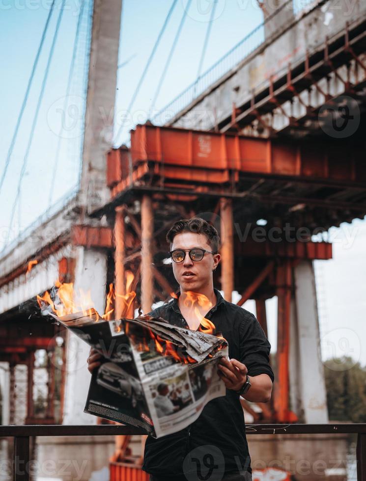 tipo legge un' ardente giornale, nel il sfondo un' ponte foto