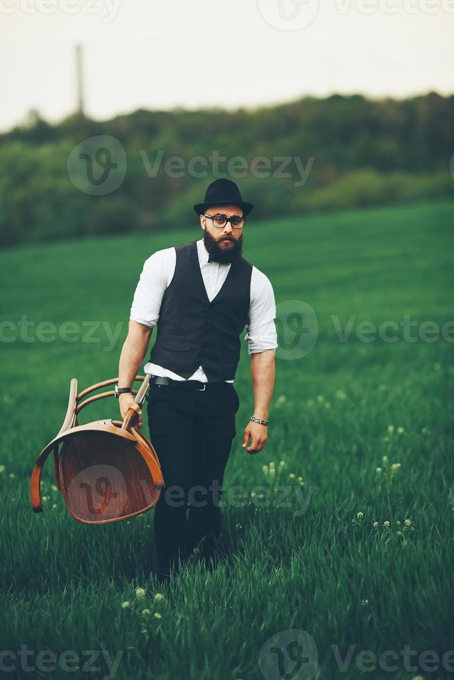 barbuto uomo trasporta un' sedia su il campo foto