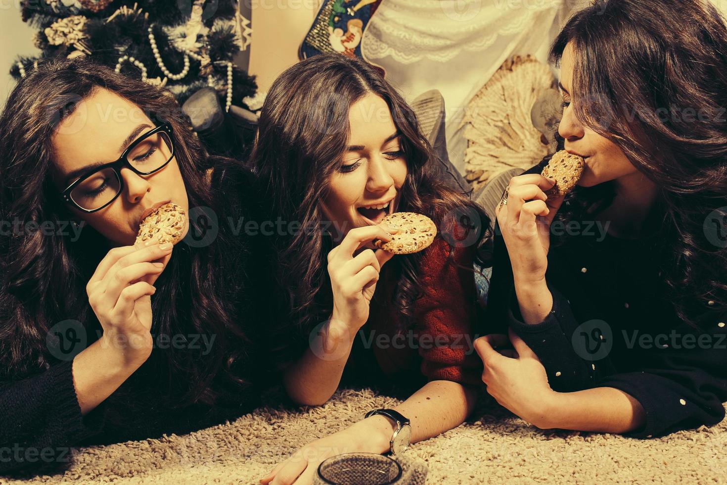 bellissimo ragazza mangiare Natale biscotti e bevanda tè mentre dire bugie su un' tappeto. decorativo Vintage ▾ appartamento. foto