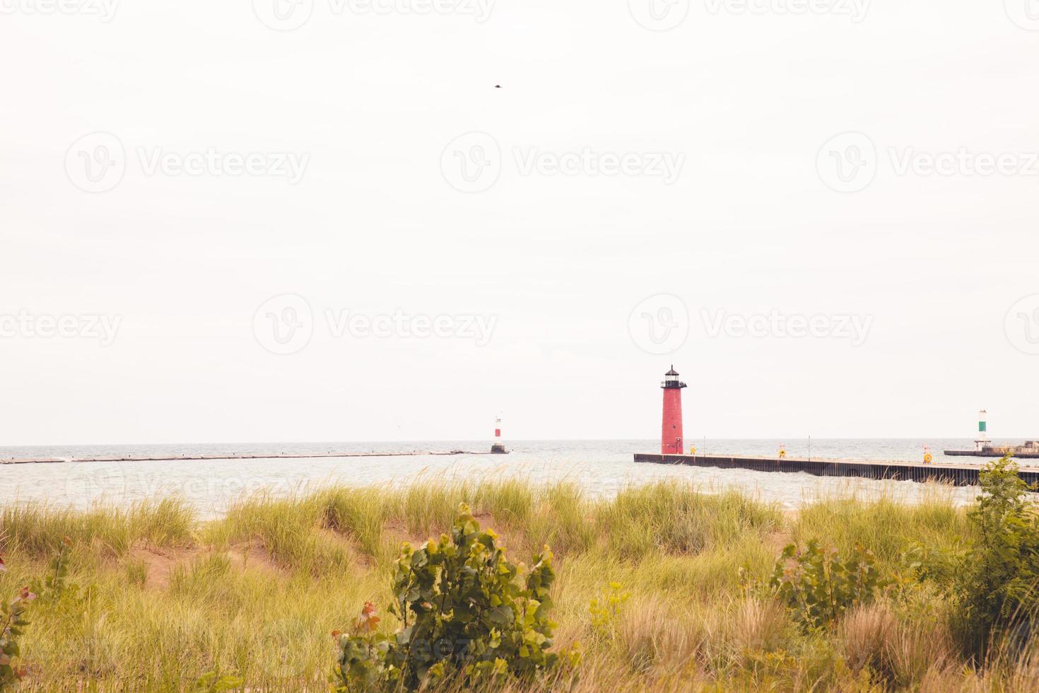 faro a fine di molo su un' nuvoloso ventoso giorno su lago Michigan. lungo molo. asciutto erbe in crescita nel il sabbia colline. rosso e verde boe marcatura il porto ingresso. foto