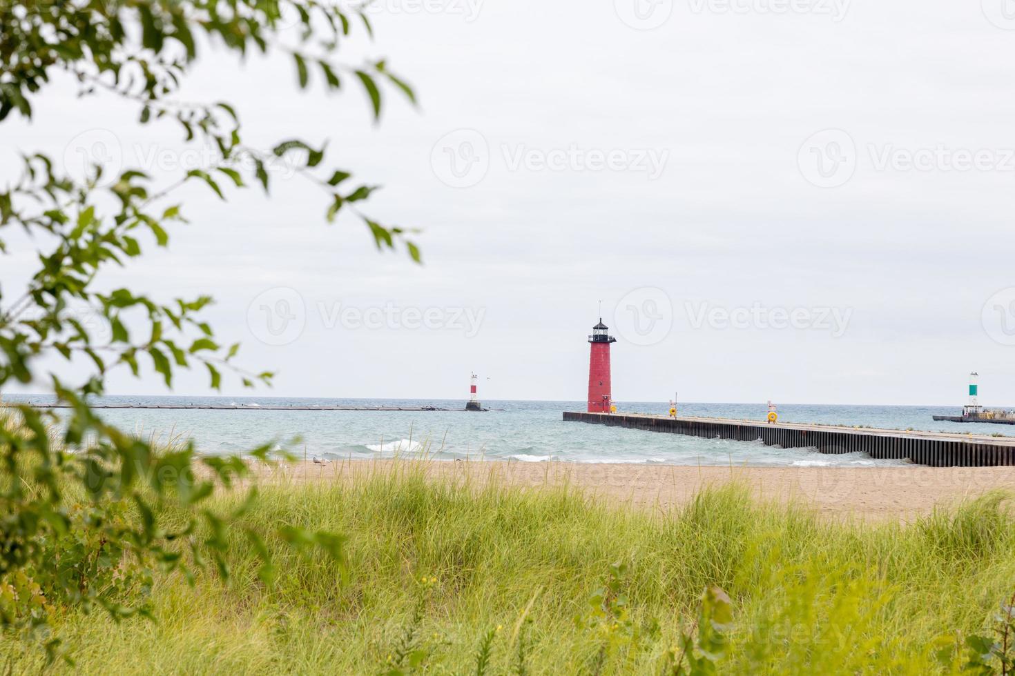 faro su il costa vicino un' bianca sabbioso spiaggia su lago Michigan. nascosto dietro a lungo erba e un' albero è un' rosso faro su un' molo nel kenosha Wisconsin dietro a un' rompere parete foto