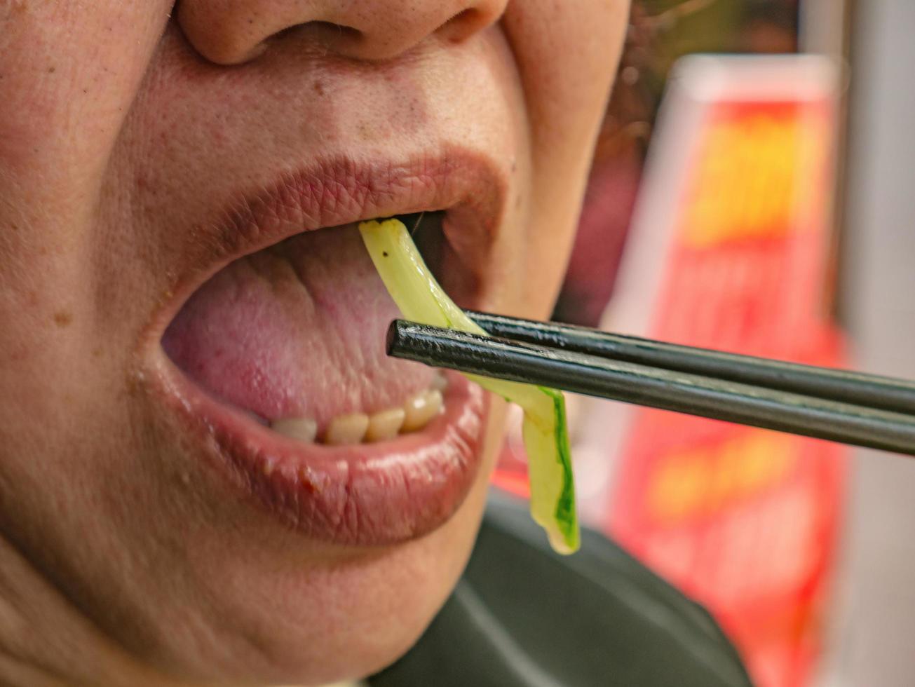 vicino su anziano asiatico donna bocca uso bacchette mangiare verdura foto