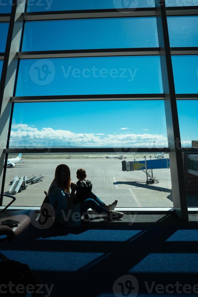 poco ragazzo e il suo madre seduta nel un aeroporto foto