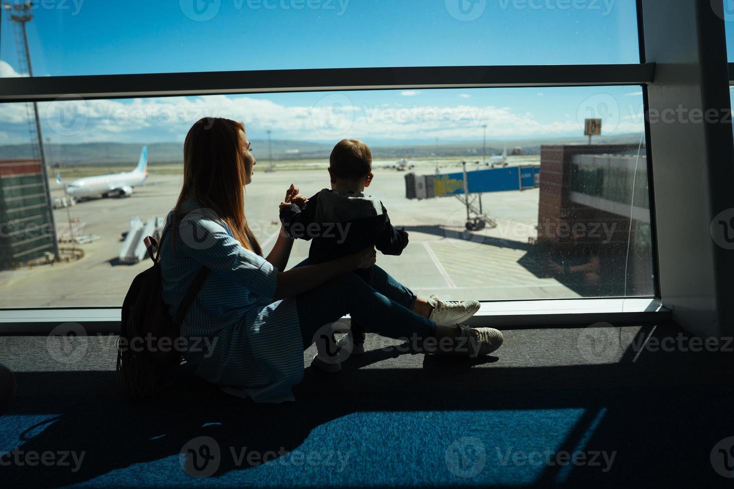 poco ragazzo e il suo madre seduta nel un aeroporto foto
