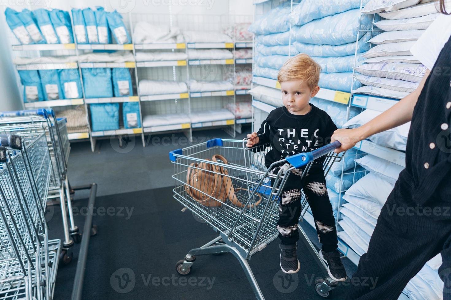 bellissimo madre trasporta sua poco figlio nel il supermercato carrello foto