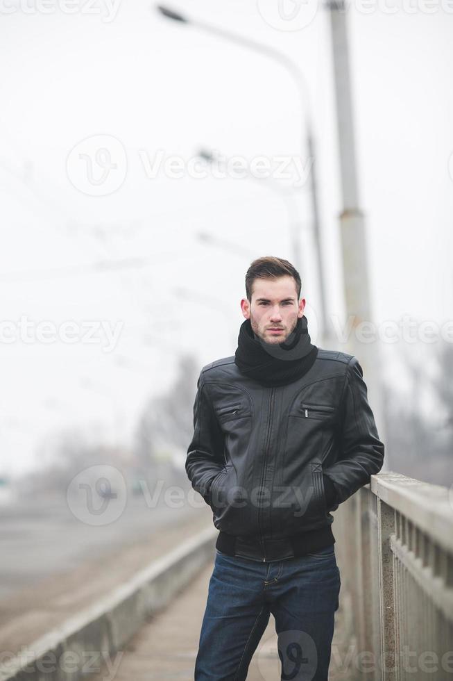 un' uomo vestito nel jeans e giacca sta vicino il principale strada nel nebbioso tempo metereologico foto