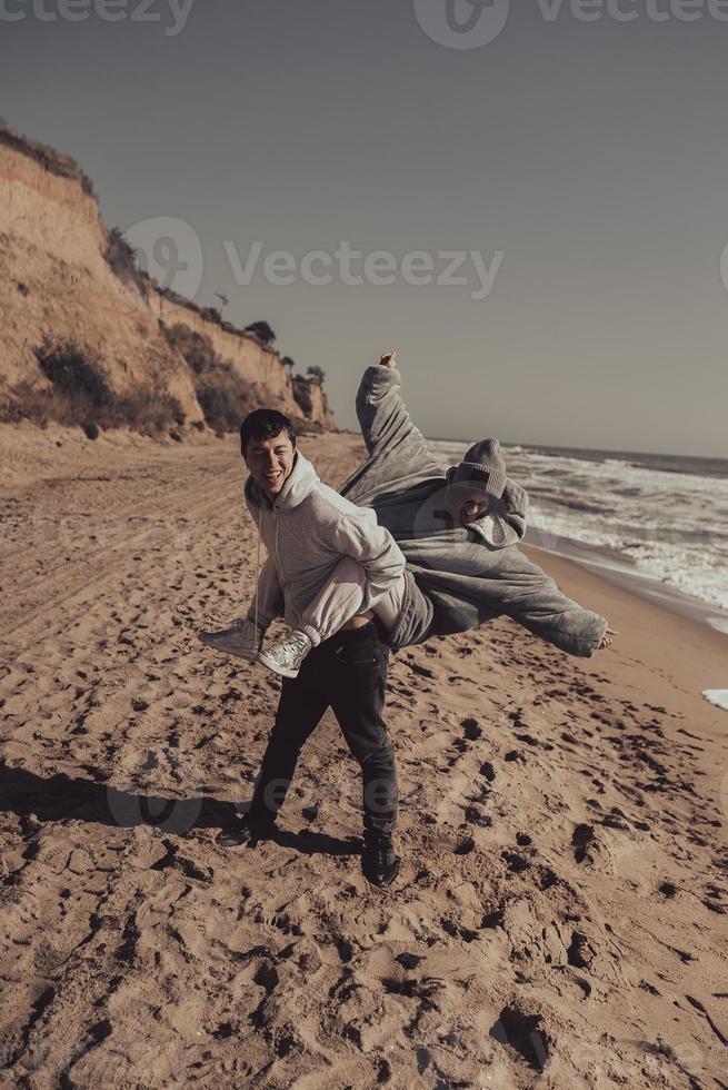 uomo trasporta il suo fidanzata su Indietro, coppia avendo divertimento su il riva del mare foto